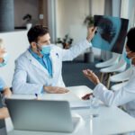 Group of doctors cooperating while analyzing X-ray of a patient at the hospital during coronavirus pandemic. Focus is on male doctor.